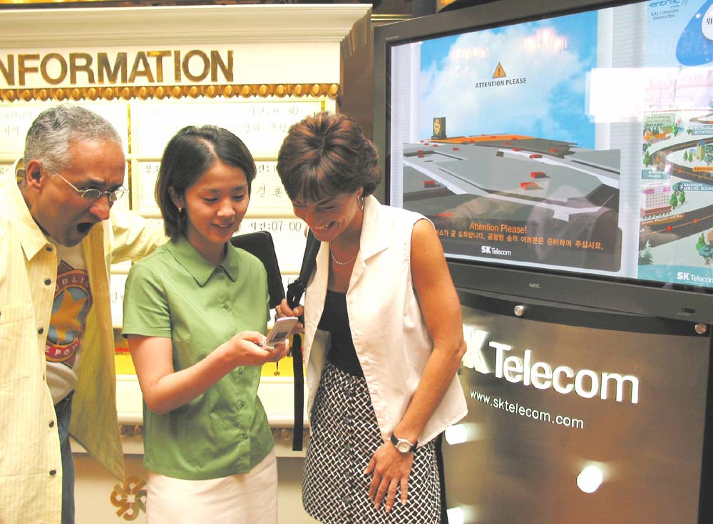 A foreign tourist is being introduced to the `Bus Location / Information Service` at the hotel lobby.
